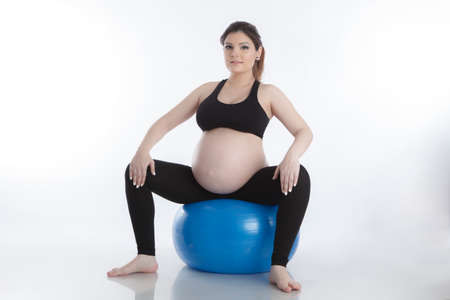 Pregnant woman is doing exercises with gymnastic ball on white backgroundの写真素材
