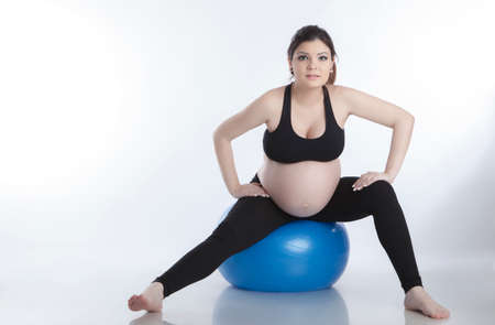 Pregnant woman is doing exercises with gymnastic ball on white backgroundの写真素材