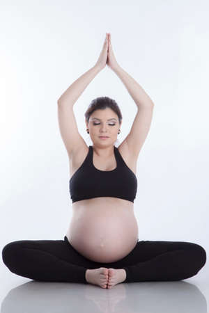 Pregnant woman relax doing yoga, sitting in lotus position over white backgroundの写真素材