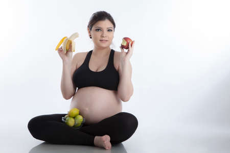 Healthy pregnant woman eating vitamin rich fruit over white backgroundの写真素材