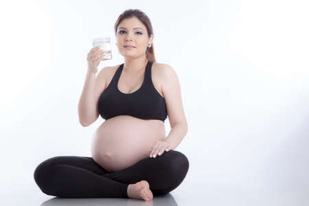Healthy pregnant woman drinking water over white backgroundの写真素材