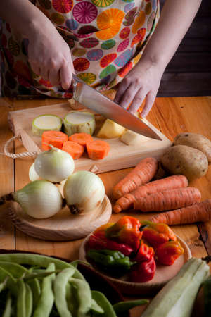 Woman prepare healthy vegetarian food with potatoes, carrots, onions, peppers, beans, chives and zucchiniの写真素材