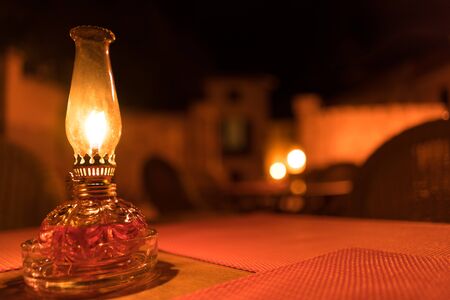 candle on a table outdoors at night standing in a square of a village with red tablecloths, chairs and out of focus backgroundの写真素材