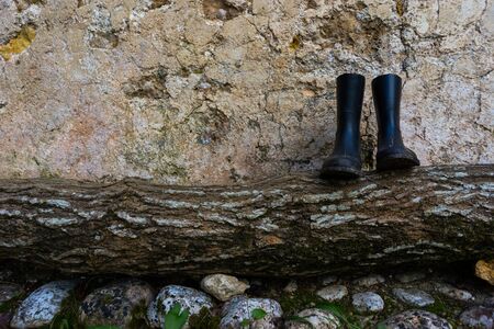 Water boots on wooden log in a rocks path on background wallの写真素材