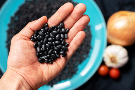 Handful of organic Black beans with a blue dish in the background, cherry tomatoes, garlic and...