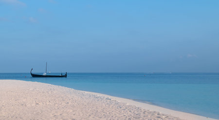 white sand beach and a sail boat over turquoise lagoon in Maldives