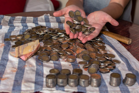 Two woman's hands holding many coins and rows of stacked coins next to many coins scattered on a...