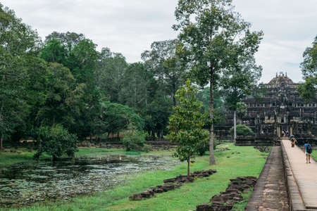 Bayon Temple in Ankgor Thom, Cambodia surrounded by a beautiful green forest, under a cloudy sky with a path of stones and tourists - World Heritage by UNESCO in 1992 - Colorful photoの写真素材