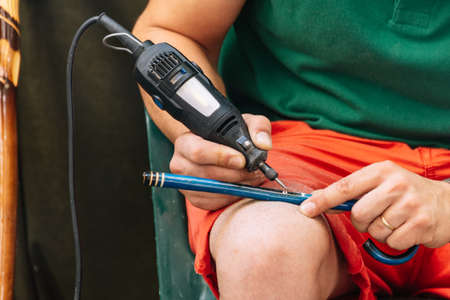 Close up of a man using a machine to make the details on a wooden stick. Hand craft present in a european fair.の写真素材
