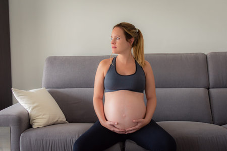 Portrait of a Beautiful pregnant woman sitting at sofa and keeping both hand on belly.の写真素材