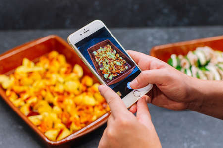 Hands taking photo baked potatoes in a casserole with smartphone. Photo of food on a smartphone.の写真素材