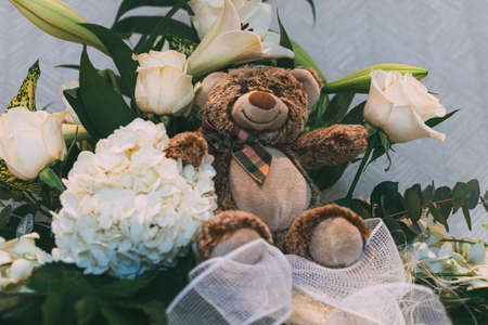Brown teddy bear between a white flowers bouquet and green leaf. White backgroundの写真素材