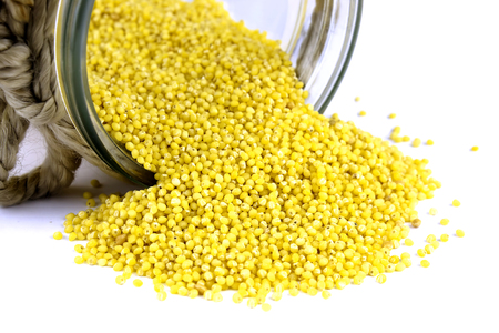 Millet groats spilling out of glass jar on backgroundの写真素材