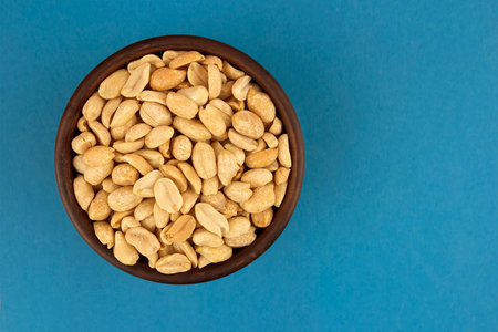 Roasted salted peanuts in bowl  on blue background, top view