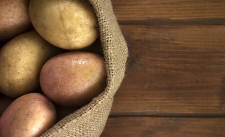 Raw potato food . Fresh potatoes in an old sack on wooden background. Free place for text. Top viewの写真素材