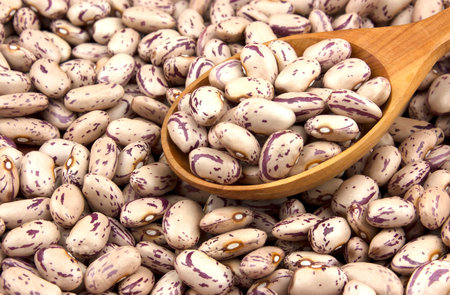 Haricot beans in a wooden spoon on white wooden background