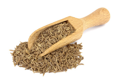 Food ingredients: heap of cumin in a wooden scoop, on white background