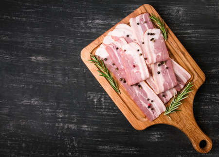Board with raw bacon with spices and rosemary on a black background, very tastyの写真素材