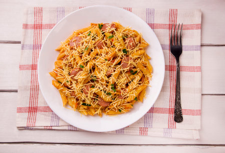 Penne pasta in tomato sauce with sausages and cheese, decorated with parsley on a white wooden...
