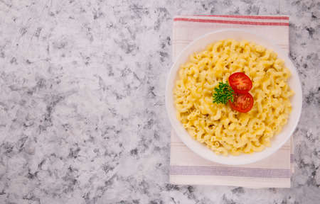 Macaroni and cheese on a white plate with parsley and cherry tomatoes on a gray background. American mac and cheeseの写真素材