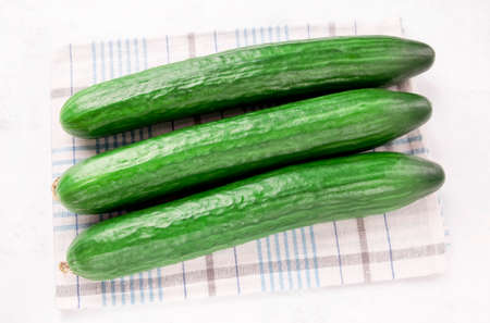 three cucumbers on a kitchen towel against a white background for a salad of spring green vegetables.の写真素材