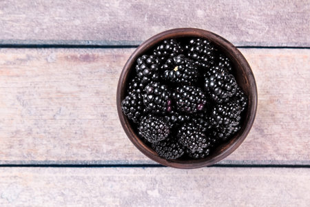 Ripe BlackBerries with Leaves in a Clay Bowl on a Light Wooden Background. Photo of BlackBerry in clay Bowl on Wooden Table.の写真素材