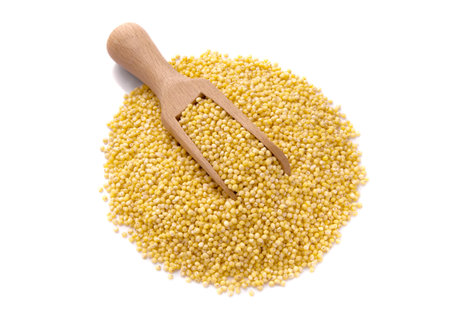Peeled yellow millet seeds in wooden scoop, organic food product isolated on white.