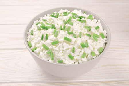 Farm cheese in a bowl on a light wooden background. Cottage cheese with young green chives. Cottage cheese in a bowl.の写真素材