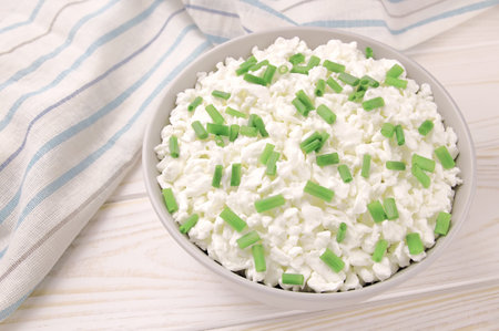 Farm cheese in a bowl on a light wooden background. Cottage cheese with young green chives. Cottage cheese in a bowl.の写真素材
