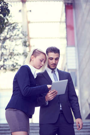 smiling businessman and businesswoman with tablet pc computer over office buildingの写真素材