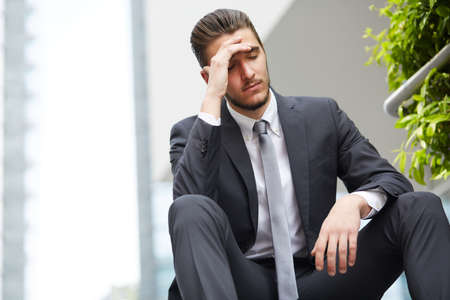 Young business man crying abandoned lost in depression sitting on ground street concrete stairs suffering emotional painの写真素材