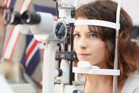 Pretty woman is looking into eye test machine with concentration in oculist lab