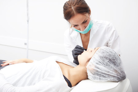Cosmetologist applying permanent make up on lips