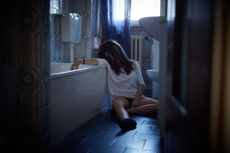 Girl addict unconscious sitting on the bathroom's floorの写真素材