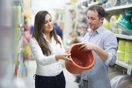 Man and woman choosing ceramic flower pot in garden shop. Focus on womanの写真素材