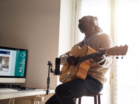 Young man is singing and playing guitar while making an audio recording at home