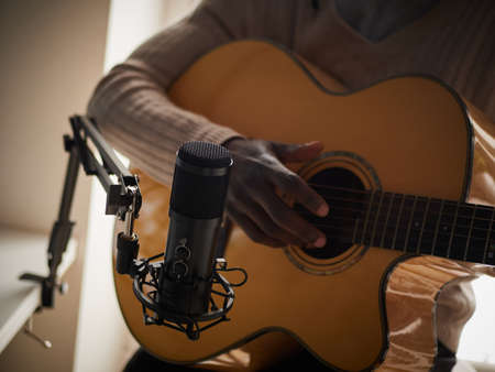 Young man is singing and playing guitar while making an audio recording at homeの写真素材