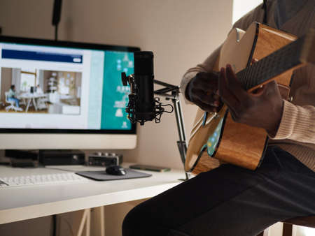 Young man is singing and playing guitar while making an audio recording at homeの写真素材
