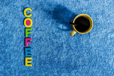 black coffee in a glass with a blue cloth background and a cork material that reads coffeeの写真素材