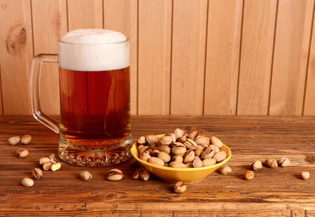Mug with light beer and pistachios on wooden tableの写真素材