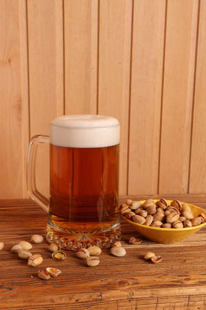 Mug with light beer and pistachios on wooden tableの写真素材