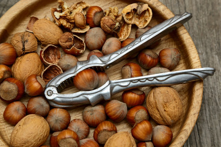 Hazelnuts, walnuts and nutcracker in a wooden bowl on a gray table. top view