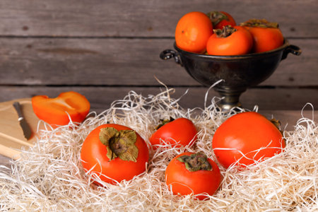 Persimmon in the straw on a wooden tableの写真素材