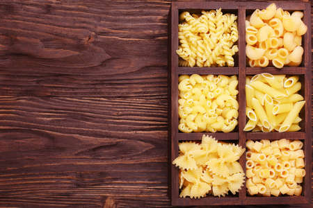 Italian pasta in assortment, several different varieties separated in a decorative box,  on a brown wooden background, place for textの写真素材
