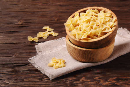 Pasta farfalle in a wooden bowl on the tableの写真素材