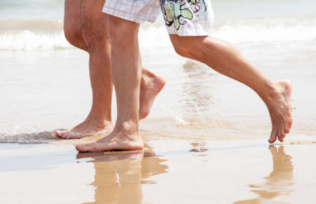 Two people walk barefoot along the shore on the sandの写真素材