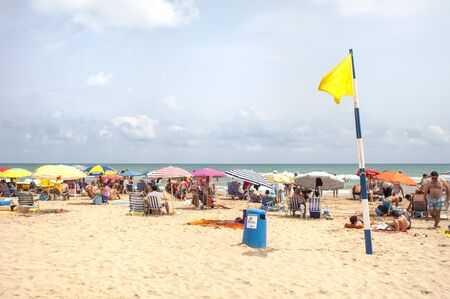 GANDIA, SPAIN-JULY 26: Unidentified people on the beach of Gandia with yellow caution flag on July 26.2012 in Gandia, Spain. With caution the bathroom is not advisable, either by the sea state or by the presence of jellyfish in the waterのeditorial素材