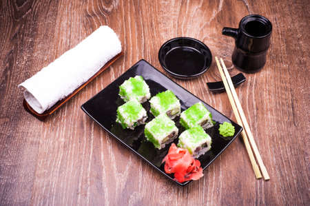sushi roll set in green caviar with ginger, soy sauce, towel and chopsticks on wooden backgroundの写真素材