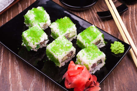 sushi roll set in green caviar with ginger and chopsticks on wooden backgroundの写真素材
