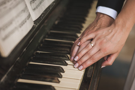 two hands with wedding rings on piano